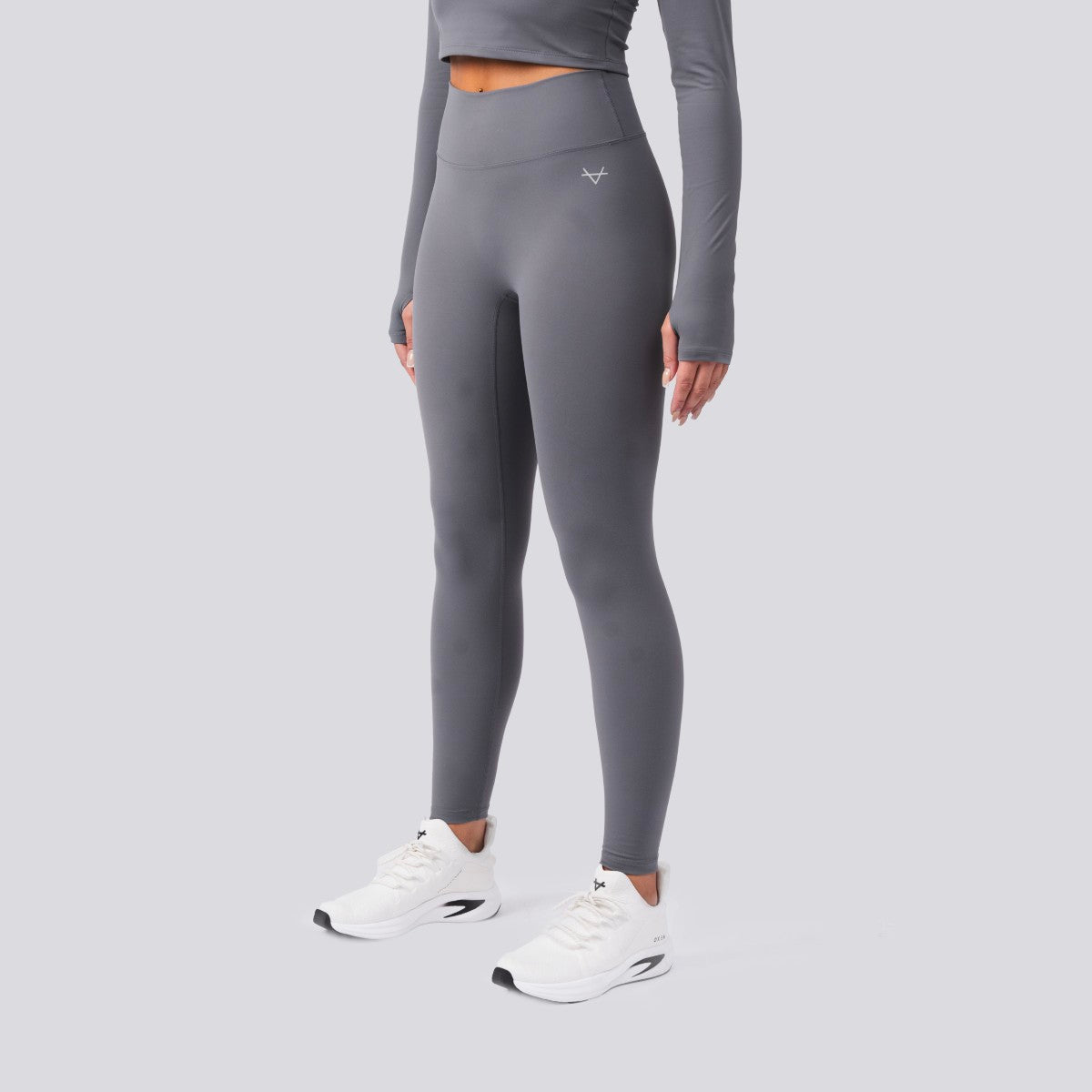 Person wearing gray athletic leggings and a long-sleeve top on a light gray background