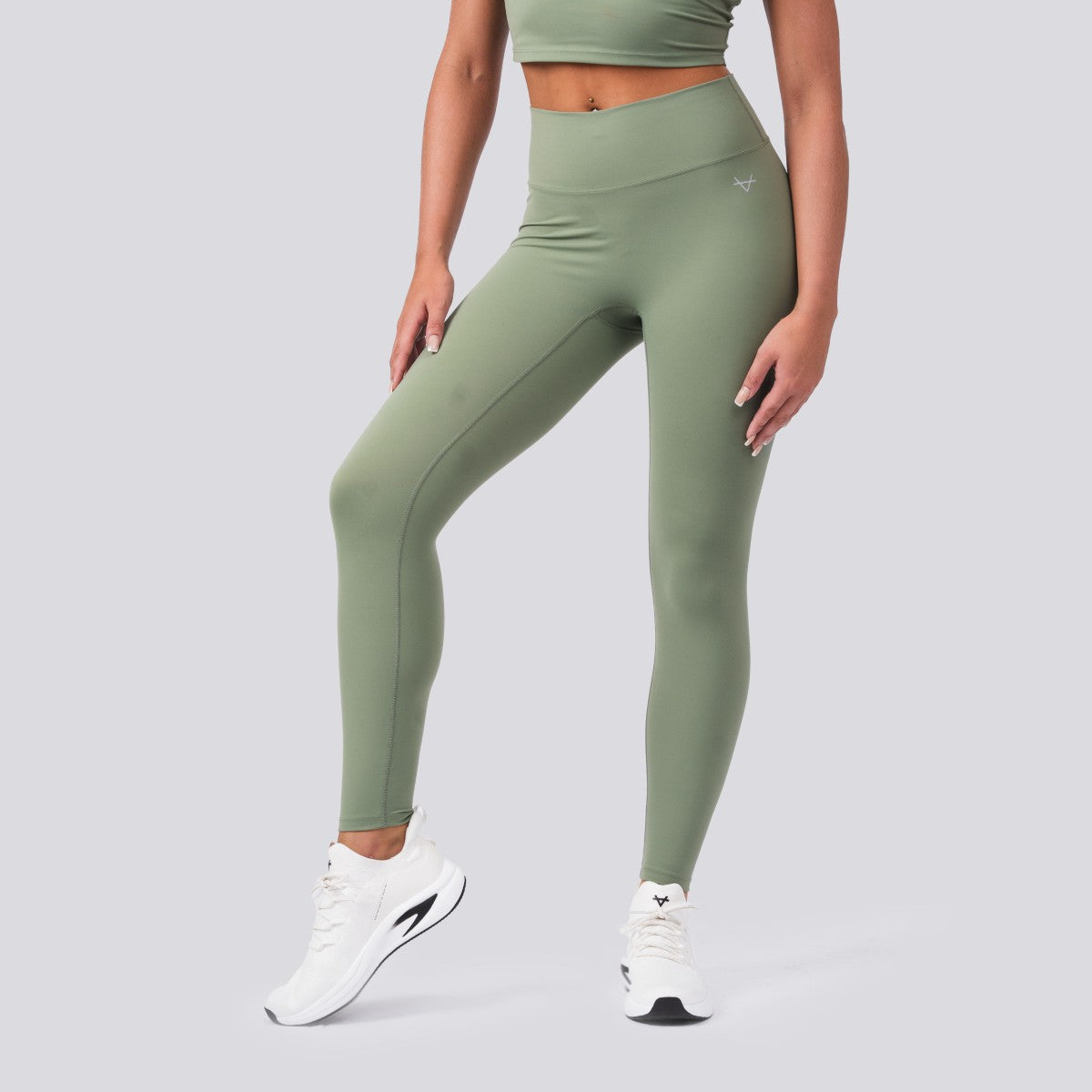 Person wearing green leggings and white sneakers on a gray background