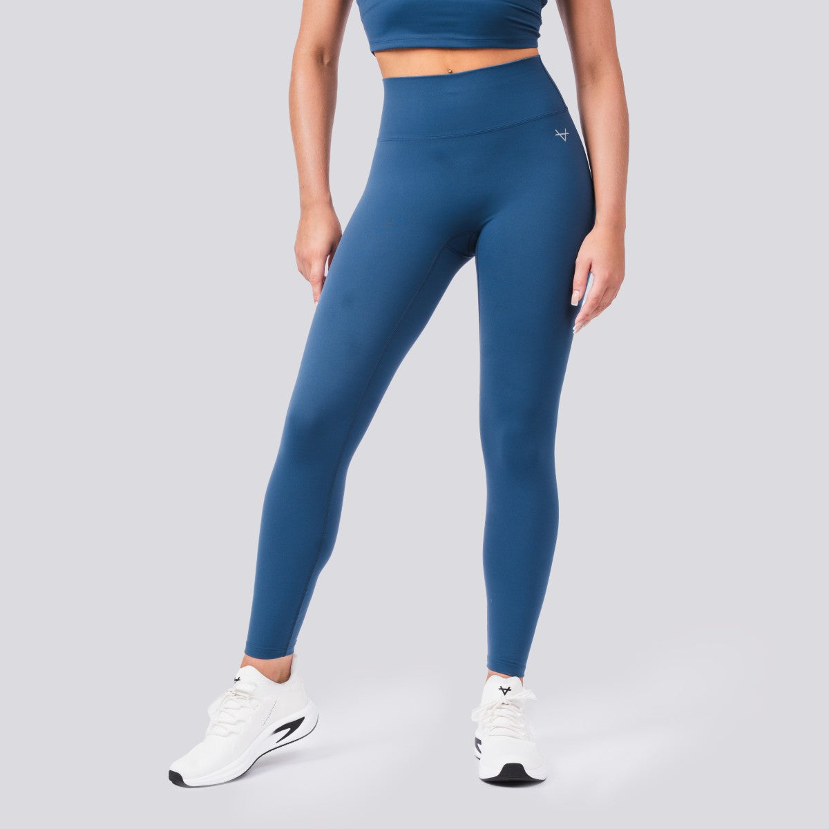 Person wearing blue leggings and white sneakers on a gray background