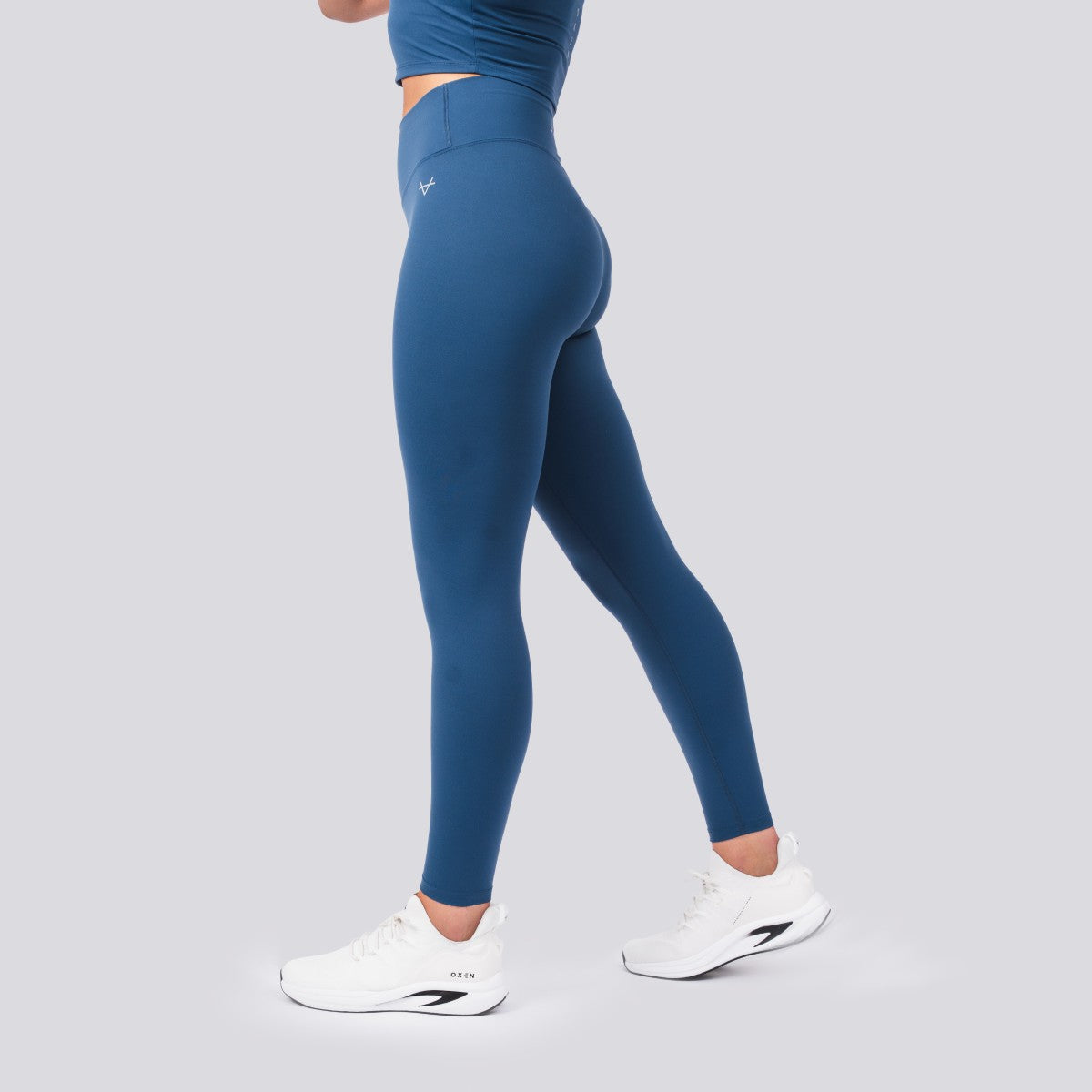 Person wearing blue leggings and white sneakers on a gray background