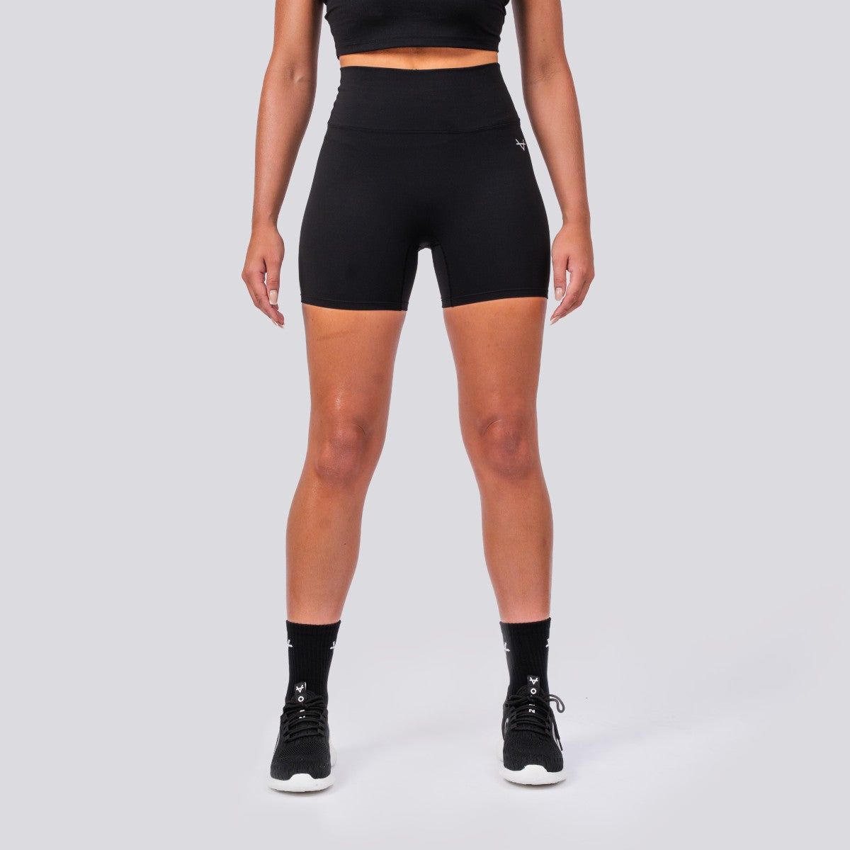 Person wearing black athletic shorts and high-top sneakers on a light gray background