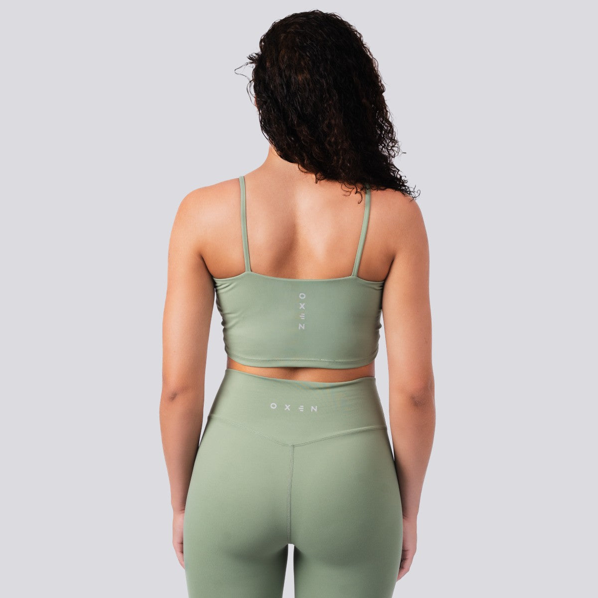 Person wearing a green sports bra and leggings set on a light gray background