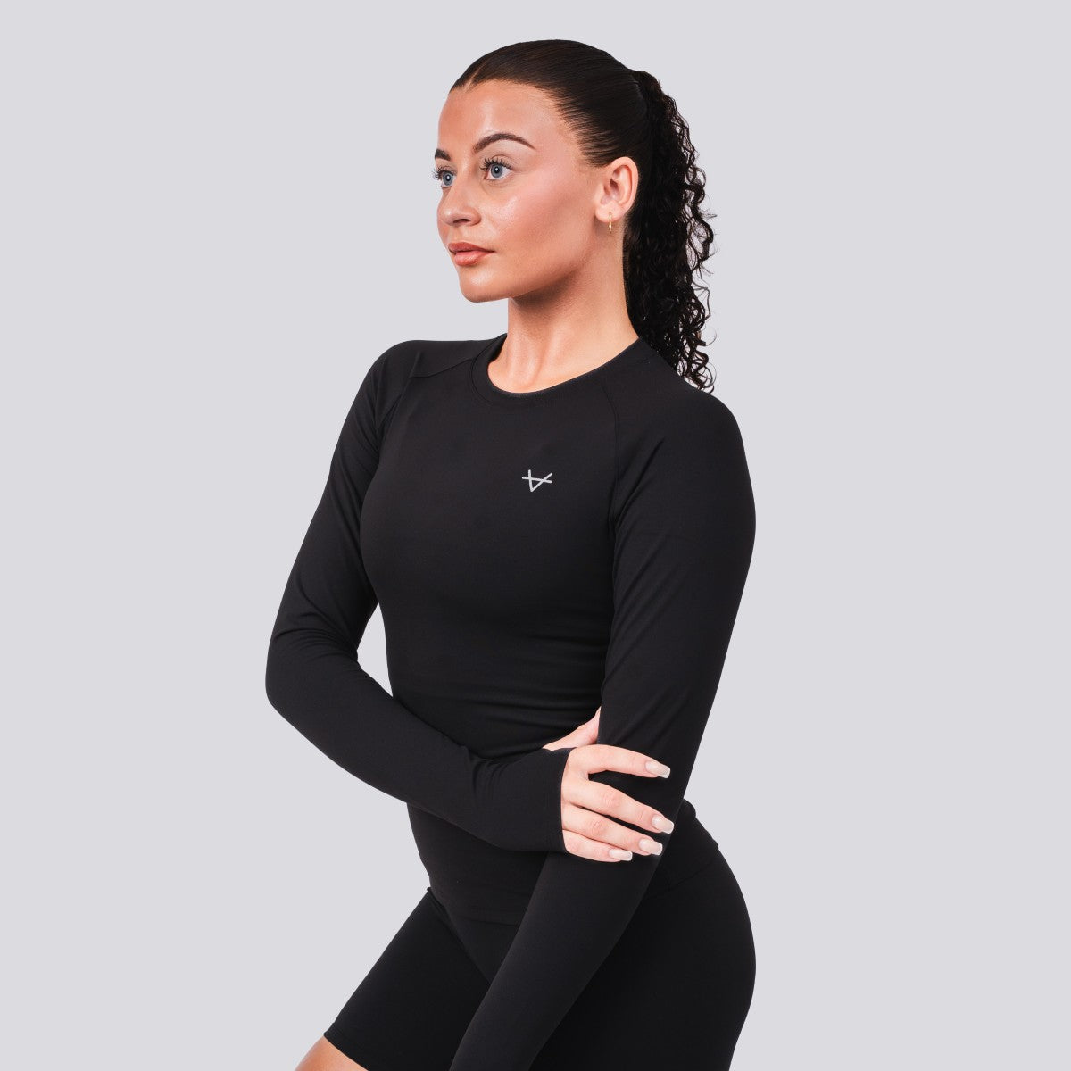 Woman wearing a black long-sleeve athletic top with a logo on a gray background