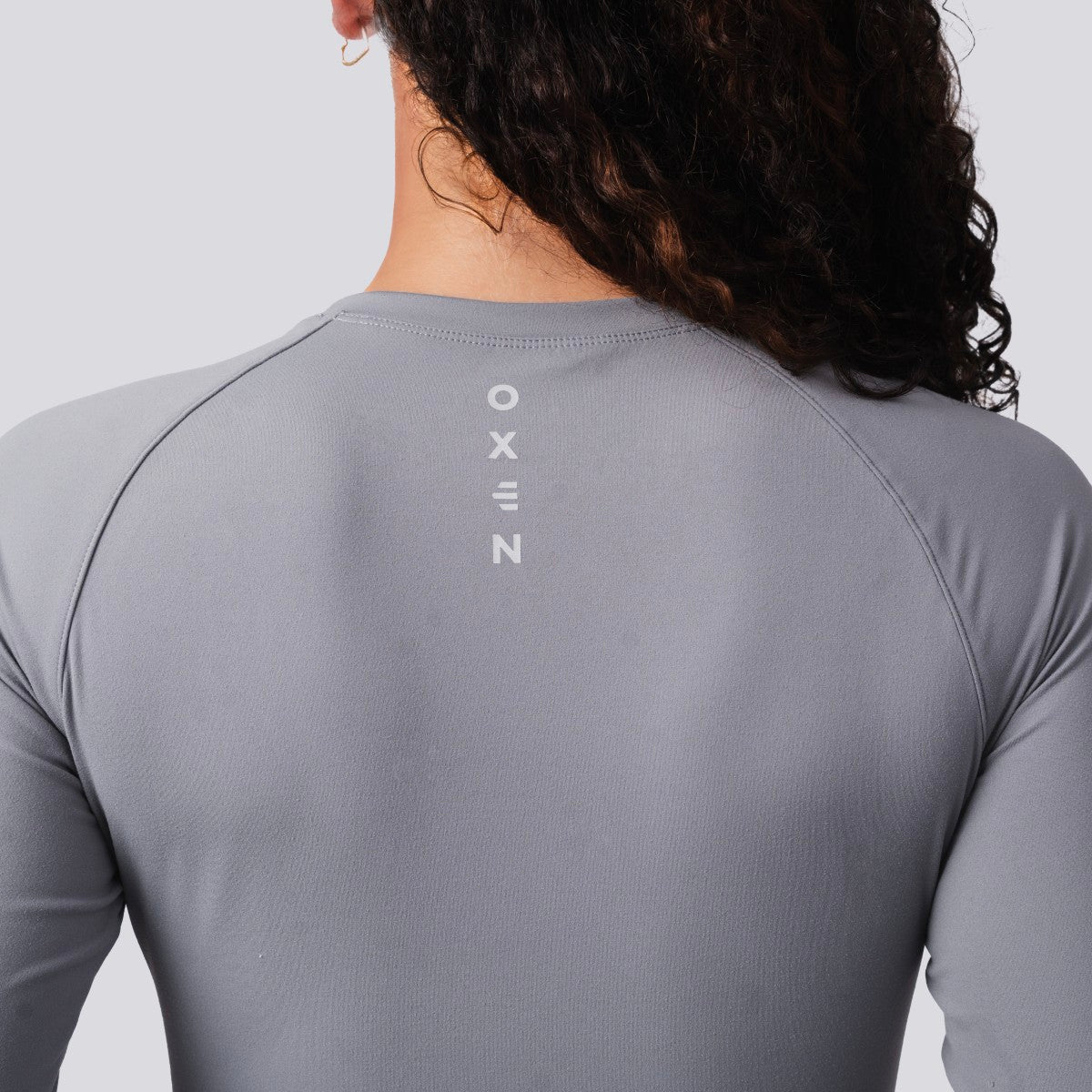 Person wearing a gray long-sleeve shirt with 'OXEN' branding on the back against a light gray background