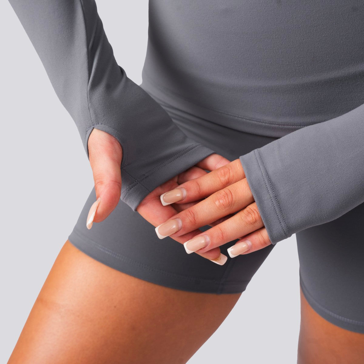 Person wearing a gray athletic outfit with long sleeves and shorts on a light gray background