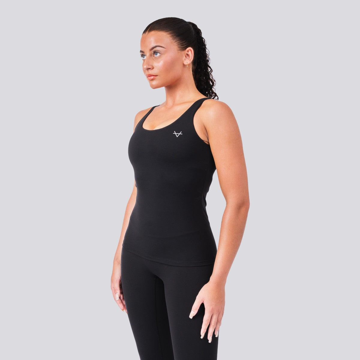 Woman wearing a black tank top and leggings with a logo on a gray background