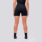 Person wearing black athletic shorts with a brand logo on a light gray background