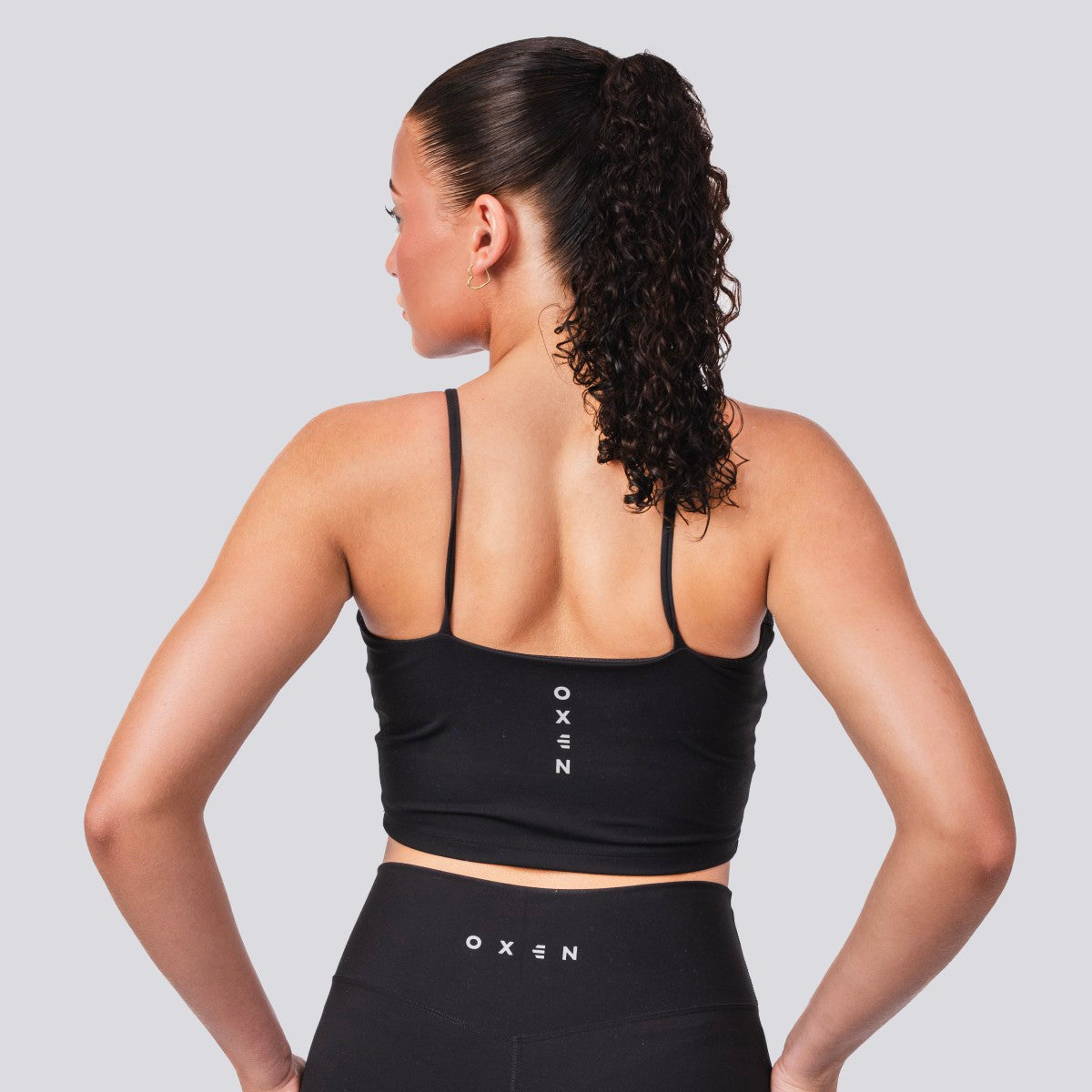 Woman wearing a black sports bra and leggings with 'OXEN' branding on a light gray background