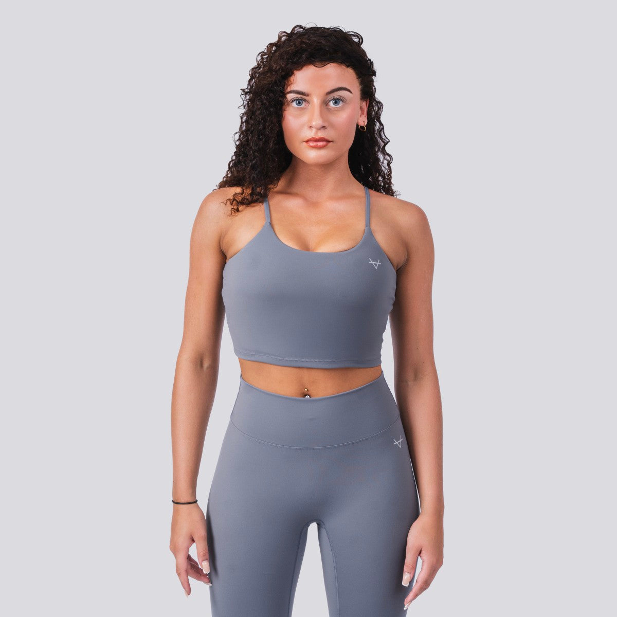 Woman wearing a gray sports bra and leggings on a light gray background