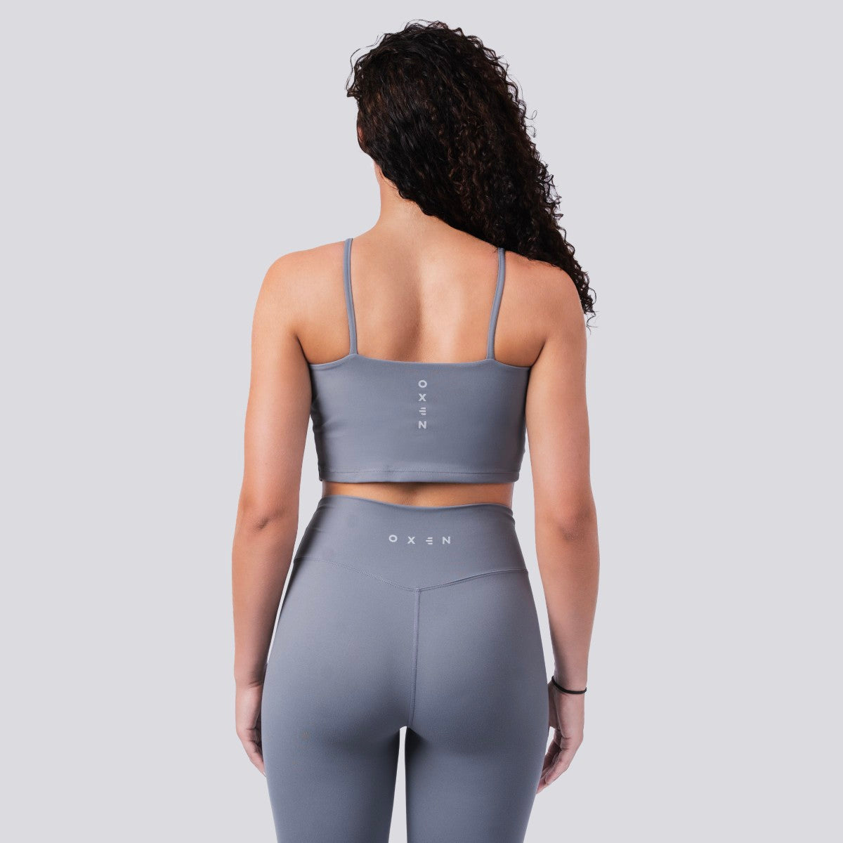 Woman wearing a gray sports bra and leggings set on a light gray background