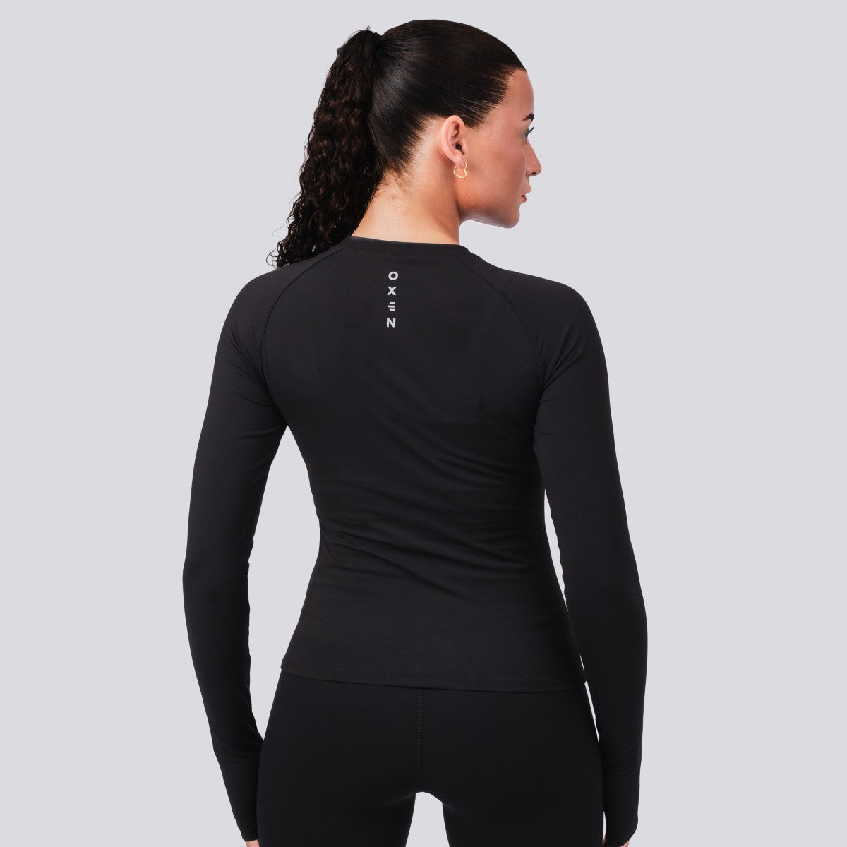 Person wearing a black long-sleeve athletic outfit with 'OXEN' branding on a gray background