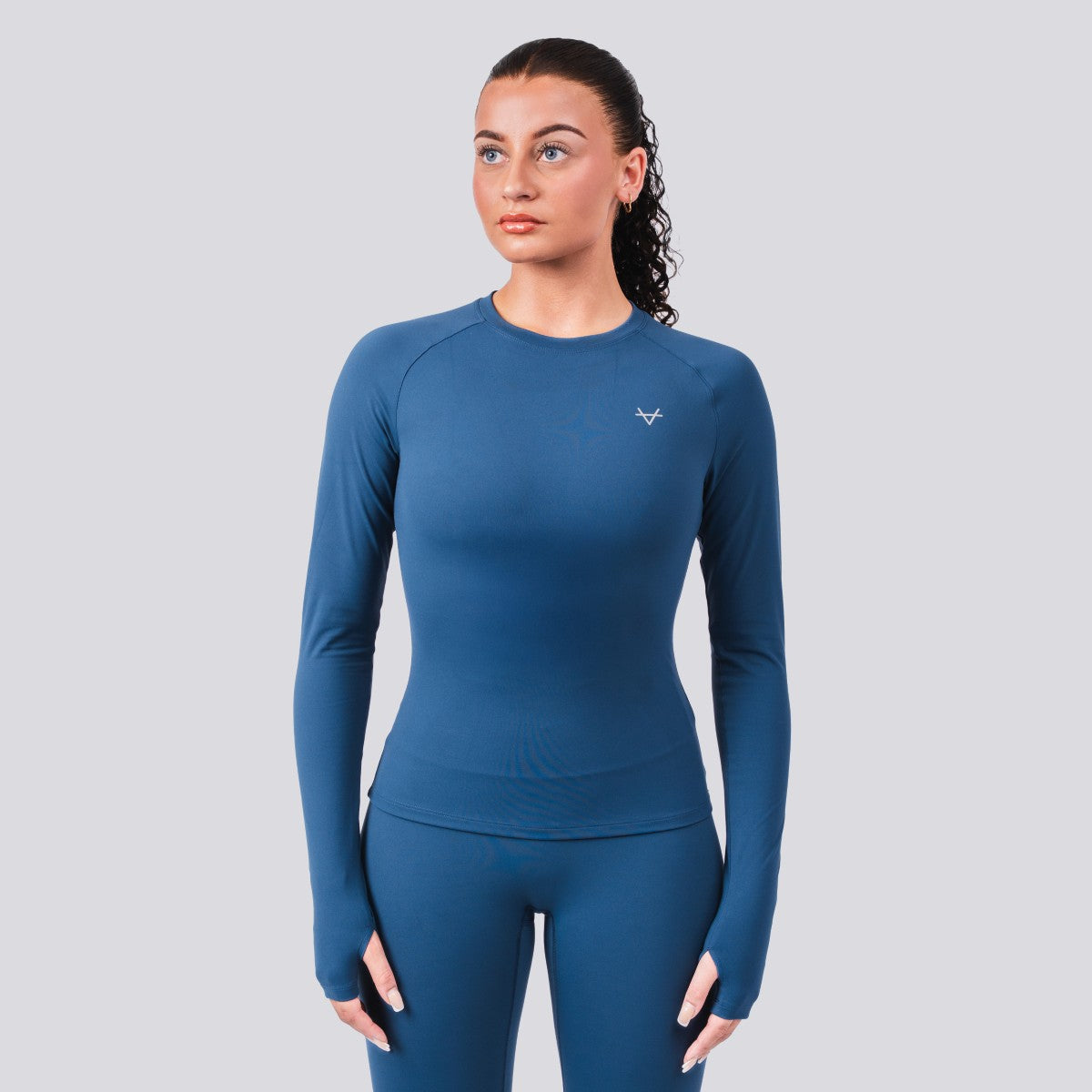 Woman wearing a blue long-sleeve athletic top and leggings on a gray background
