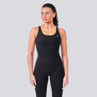 Woman wearing a black tank top and leggings on a gray background