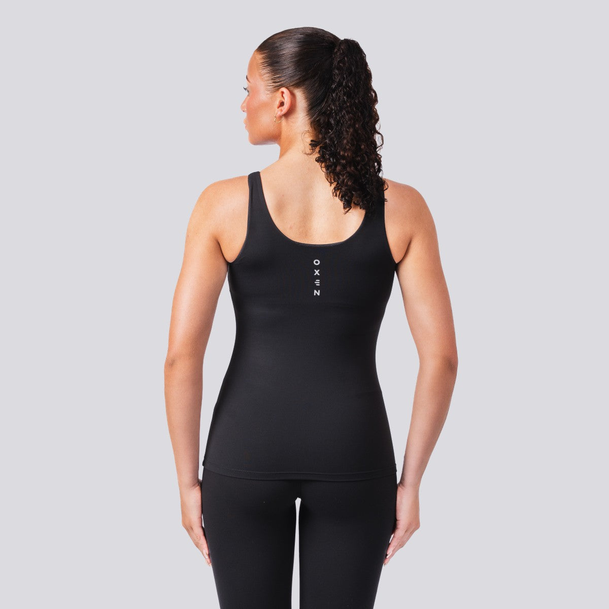 Woman wearing a black tank top with a brand logo on a gray background